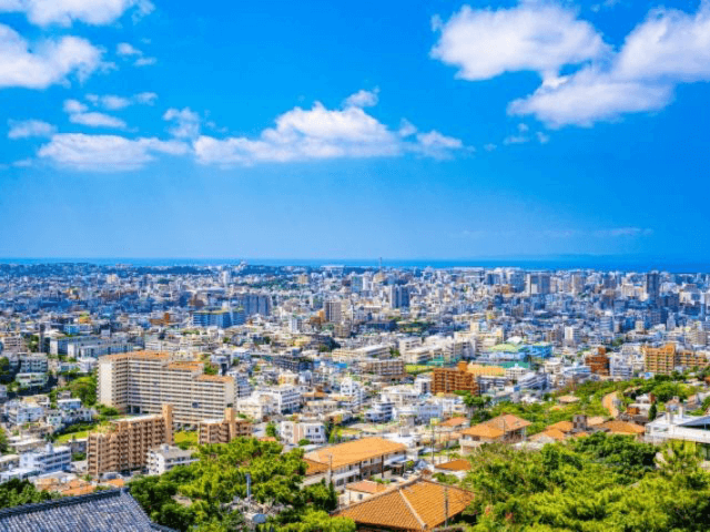 沖縄の青空と調和する、伝統的な赤瓦屋根の木造住宅が立ち並ぶ風景。