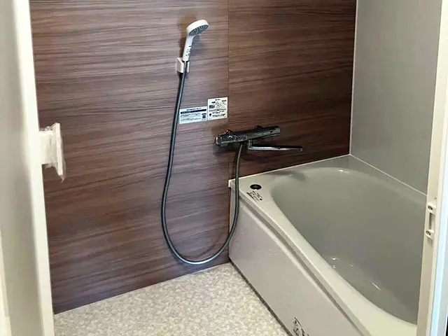 リフォーム後のユニットバス。木目調アクセントパネルと白い浴槽、シャワー水栓を設置した浴室全景。