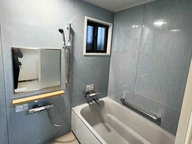 沖縄のお風呂リフォーム後のユニットバス全体写真。ブルーグレーの壁パネルと白い浴槽で明るく清潔感のある空間に一新。